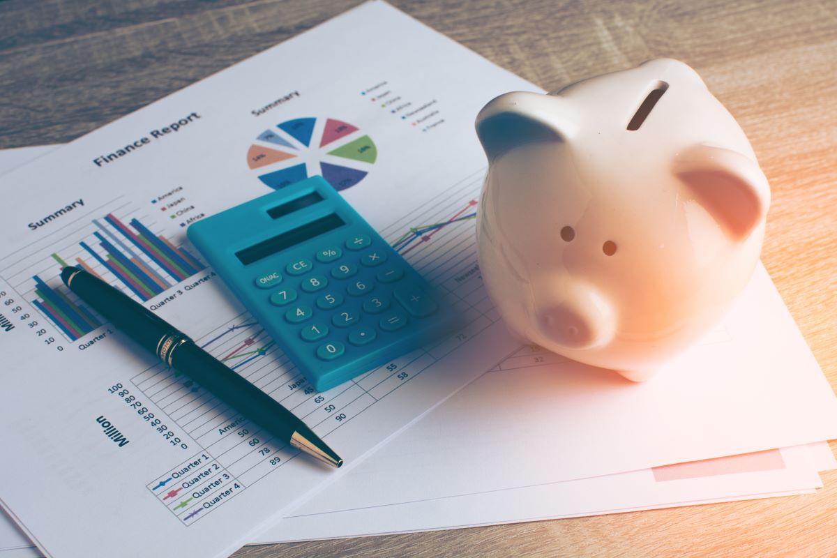 a pen a calculator and a piggy bank on top of printed graph reports