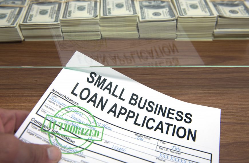 signed small business loan application being passed on a window with a great amount of money stacked