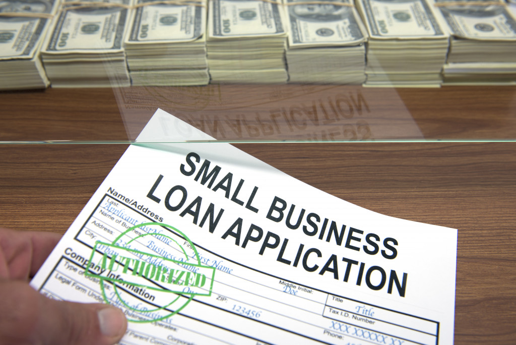 signed small business loan application being passed on a window with a great amount of money stacked