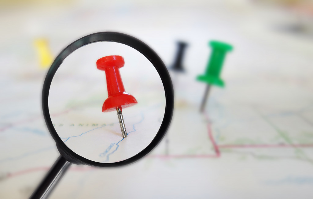 A magnifying glass over a red pin among others on a paper map