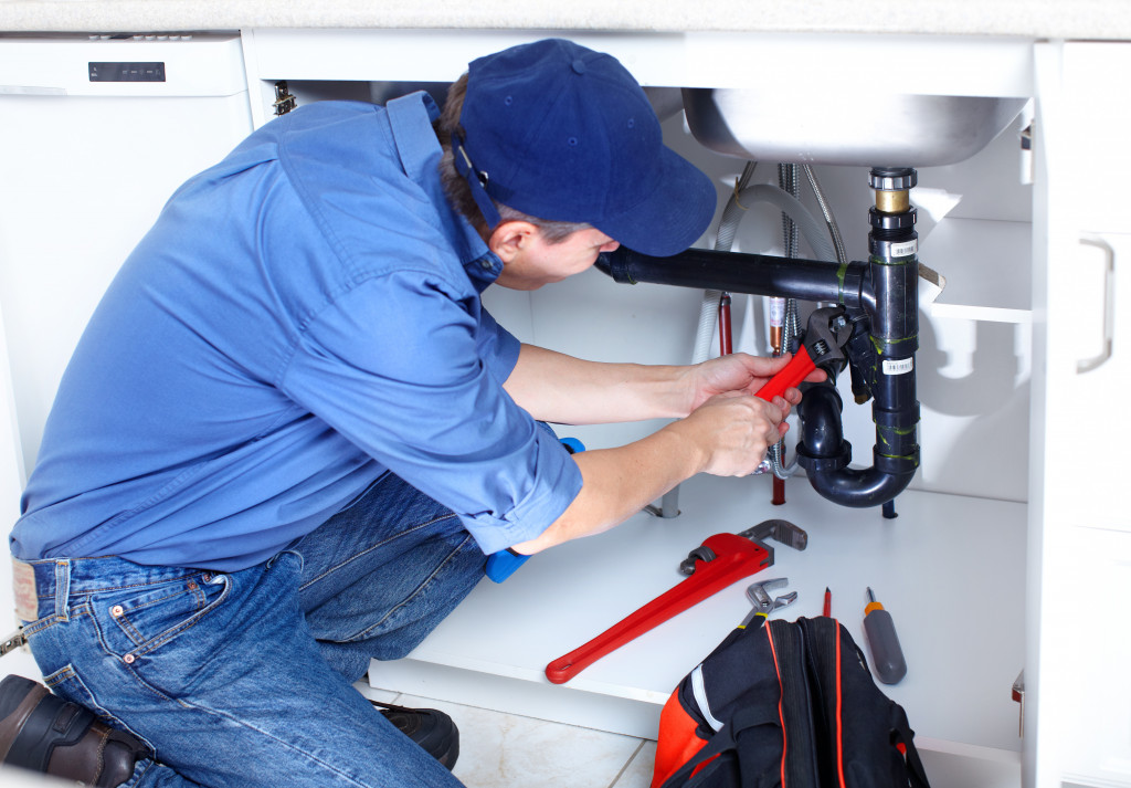 a male plumber fixing pipes under the sink