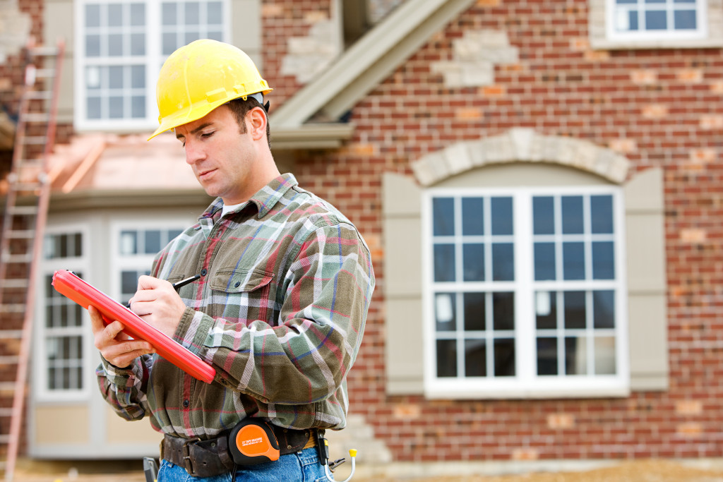 A home inspector wearing a hard hat and writing on a document in front of a house