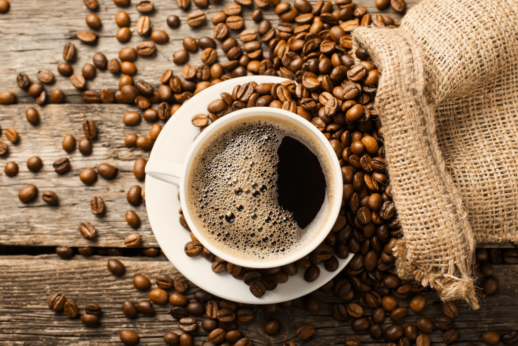 A cup of coffee and a bag of spilled coffee beans on a wooden table