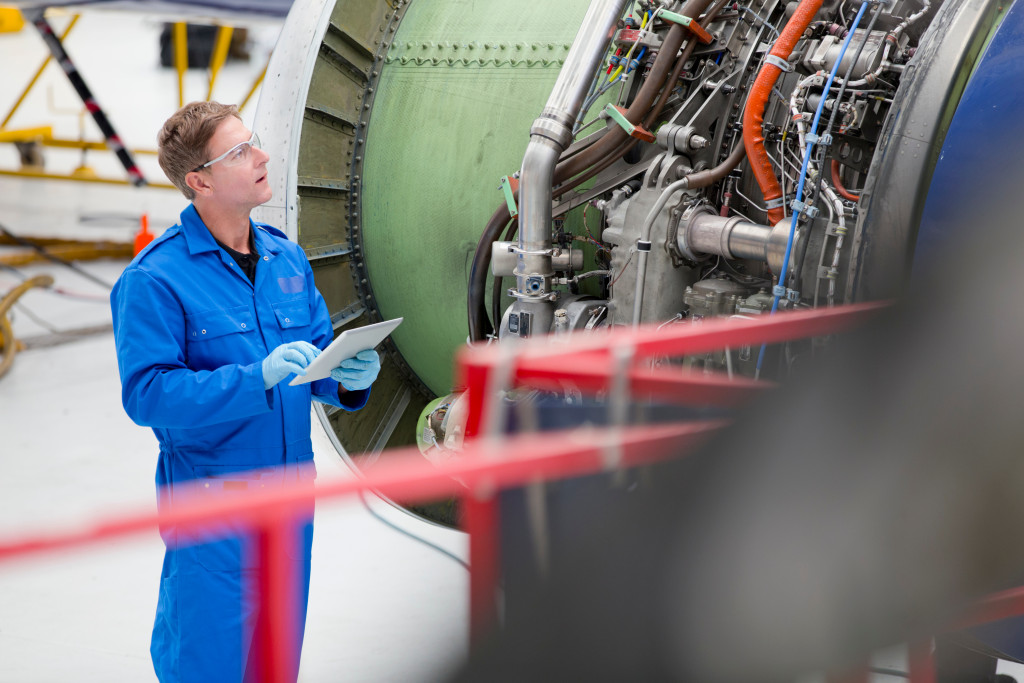 an engineer in blue uniform holding a clipboard checking and inspecting the engine of an aircraft