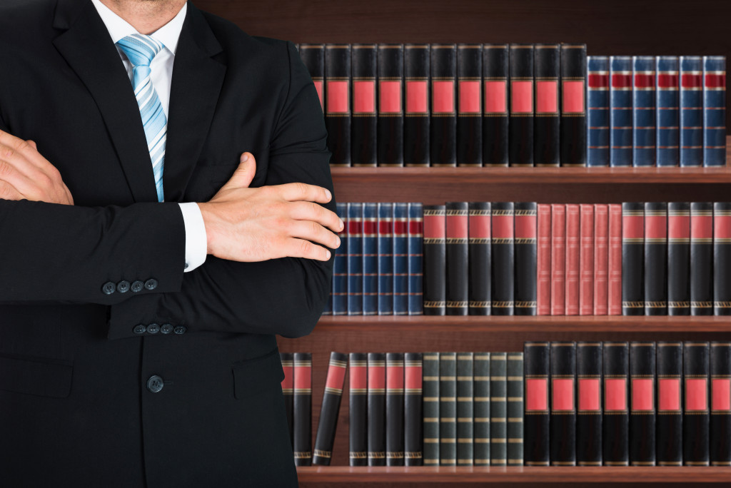 a male attorney with his arms crossed in front of a bookshelf filled with law books