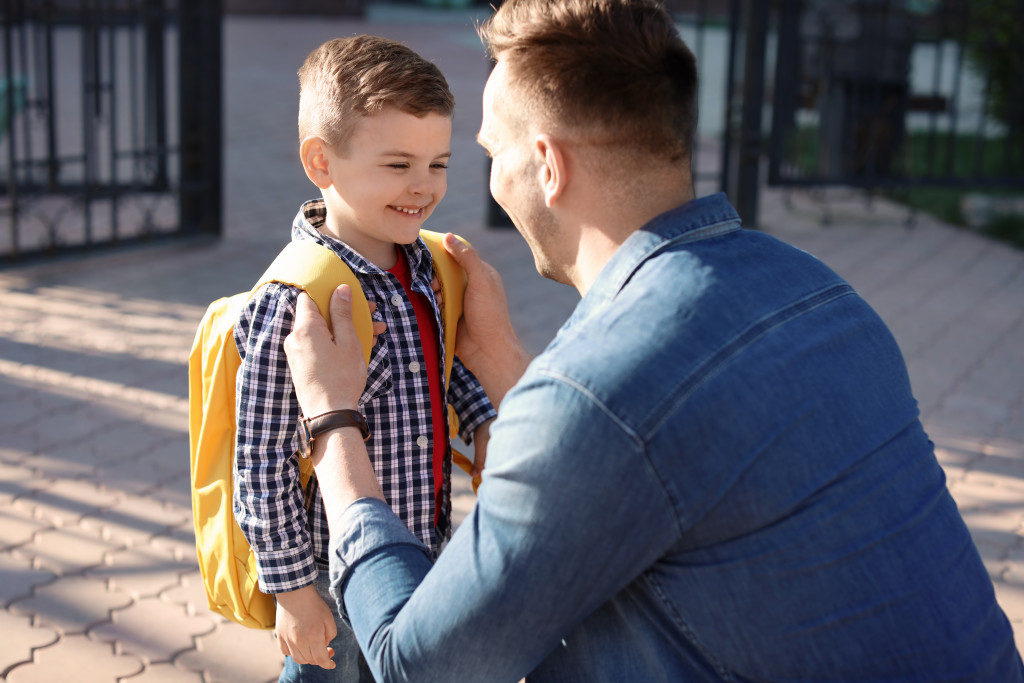 man taking young son to school with yellow backpack in the morning