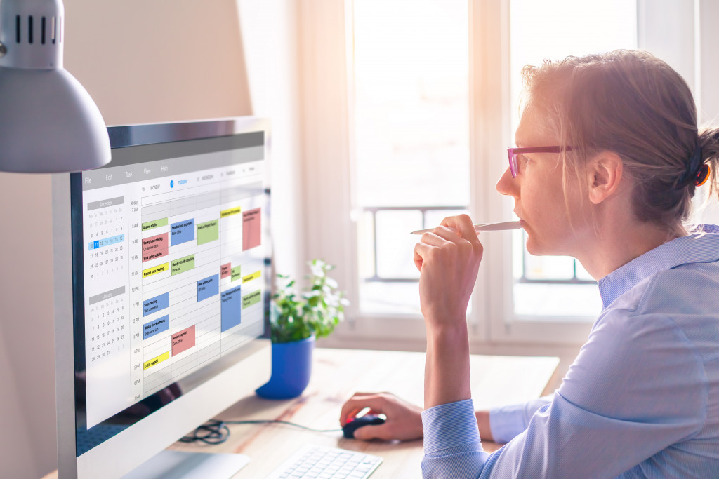 woman with glasses chewing pen while looking at schedule in desktop computer