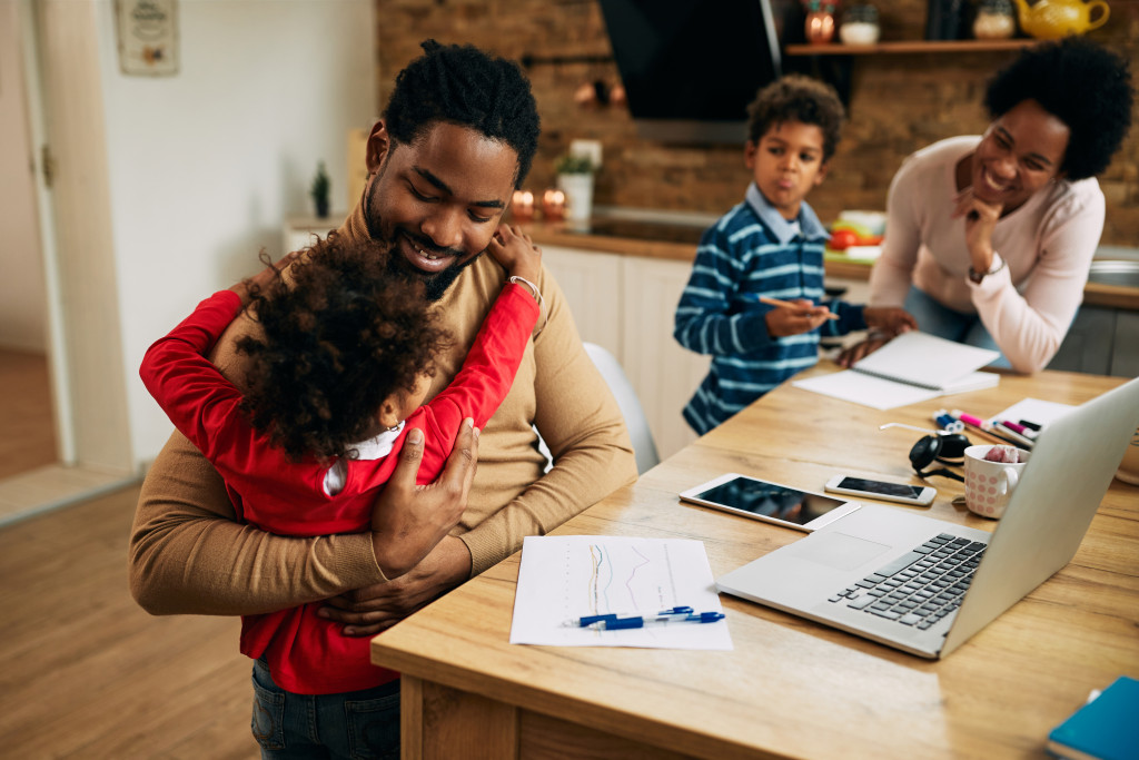 father working with laptop hugging one of his children at home