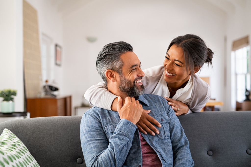 Mature couple talking with each other with the man on the couch and woman behind him.