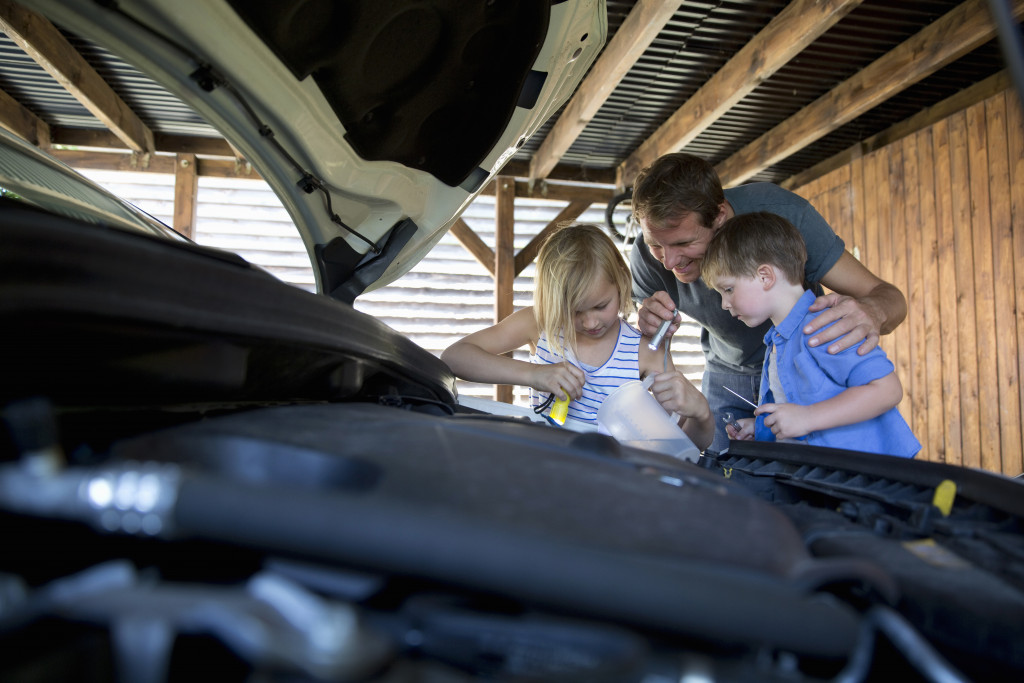 Children helping their father fix a car in the garage