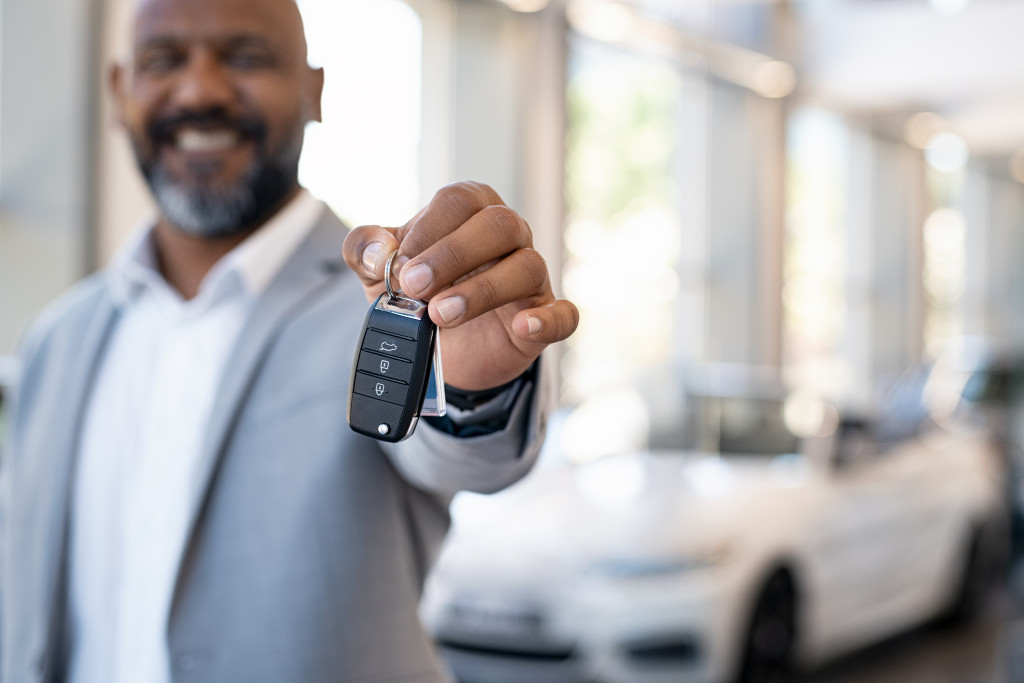 smiling car salesman handing over a car key with cars blurred in the background