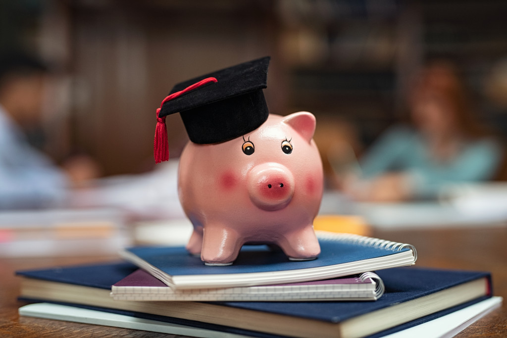 Saving money for college with piggy bank on books in library.